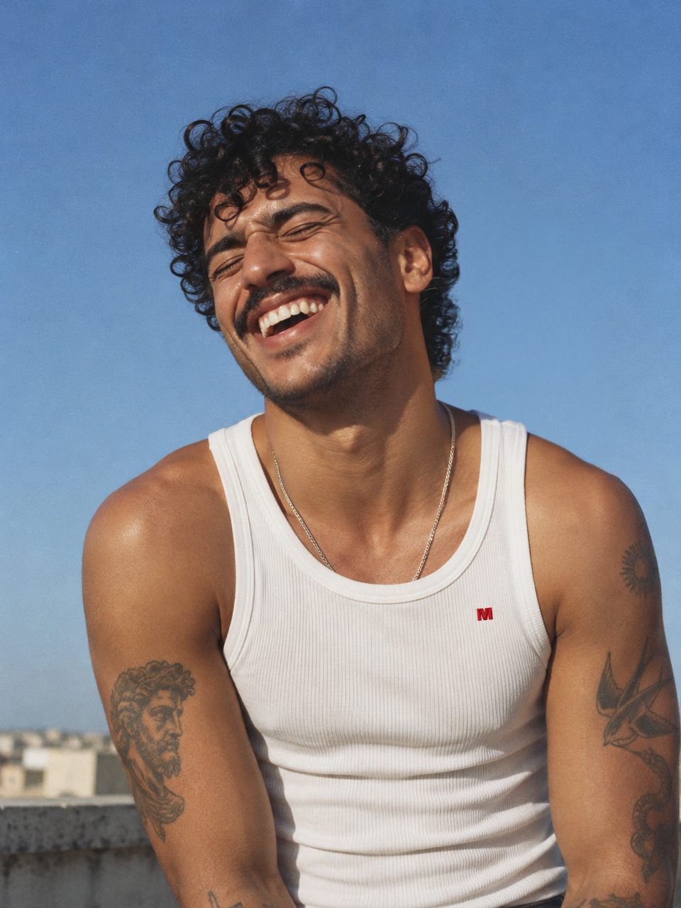 A man with curly hair laughing in a Marcelleke